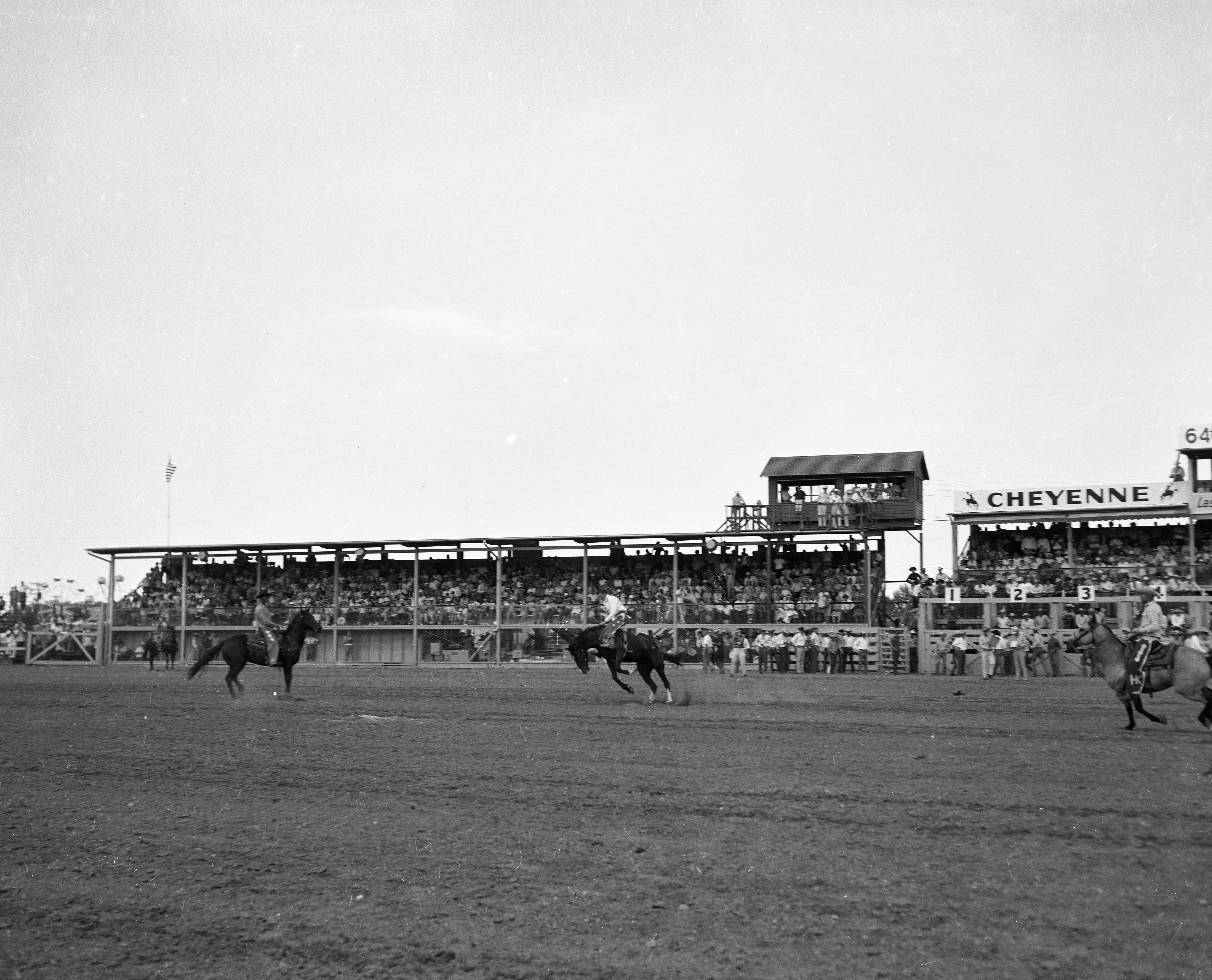 Men riding horses in rodeo arena at Frontier Days celebration.