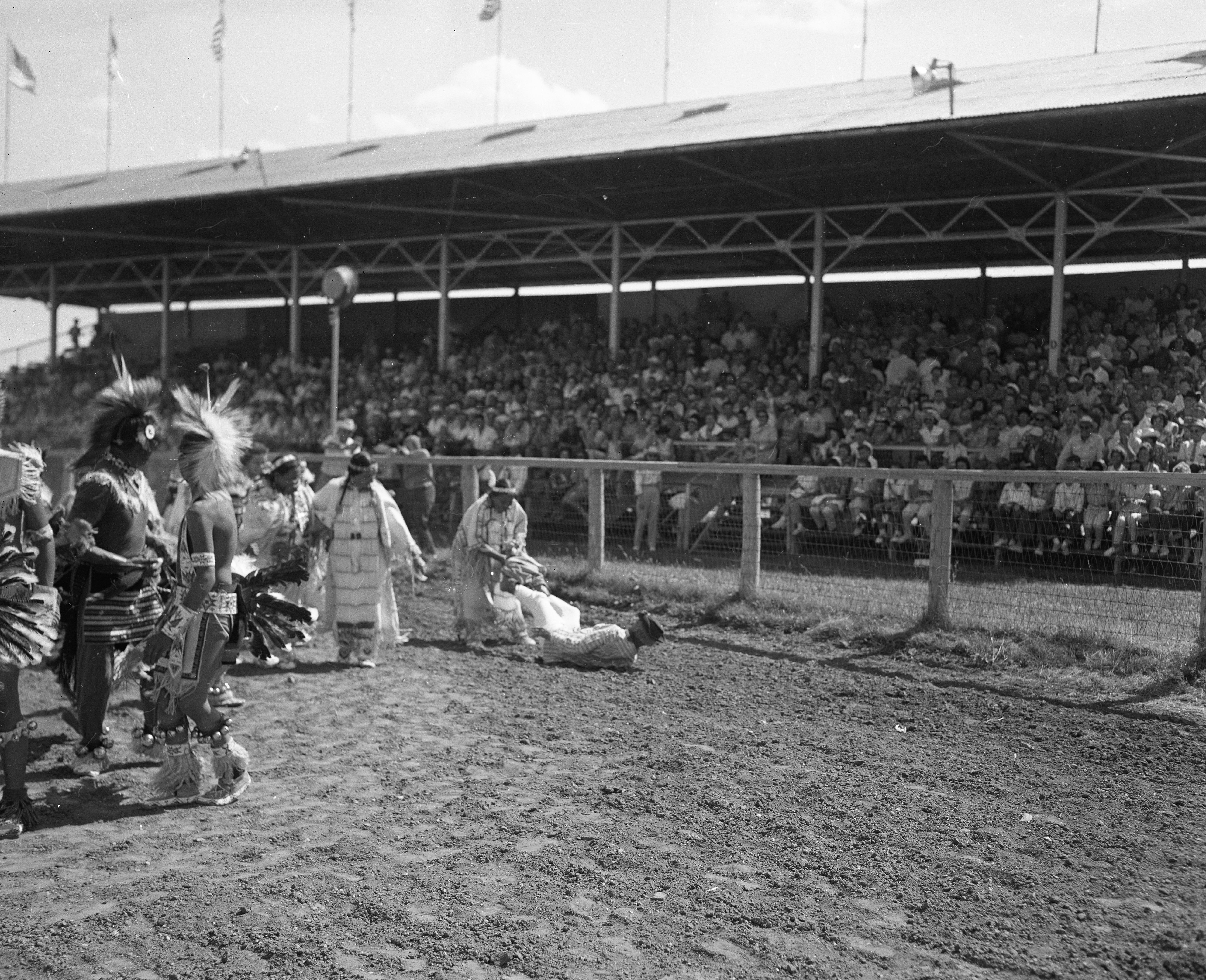 Rodeo clown interacting with Indigenous tribe member in traditional clothing.